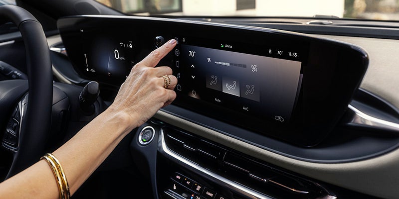 Image of the interior front dashboard of a 2024 Buick Envista with a woman's arm reaching for a button on the center touchscreen